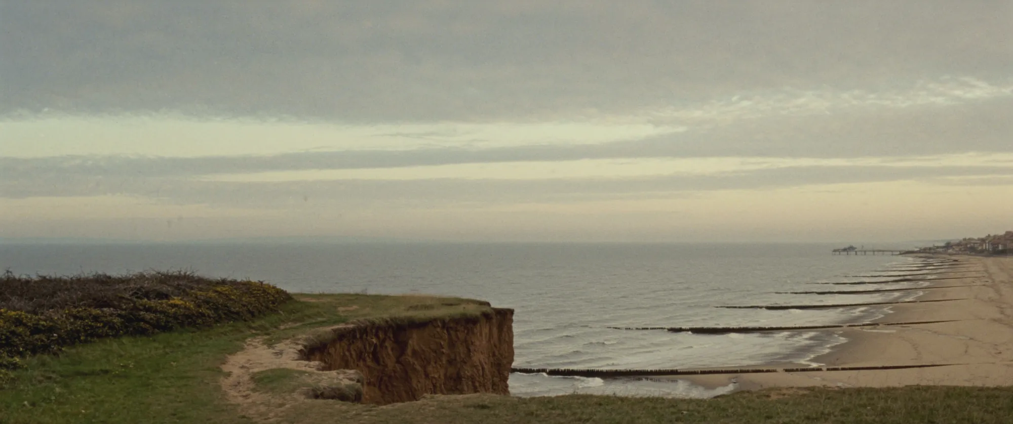Sandy cliffs and a long beach with wooden groynes under a soft evening sky
