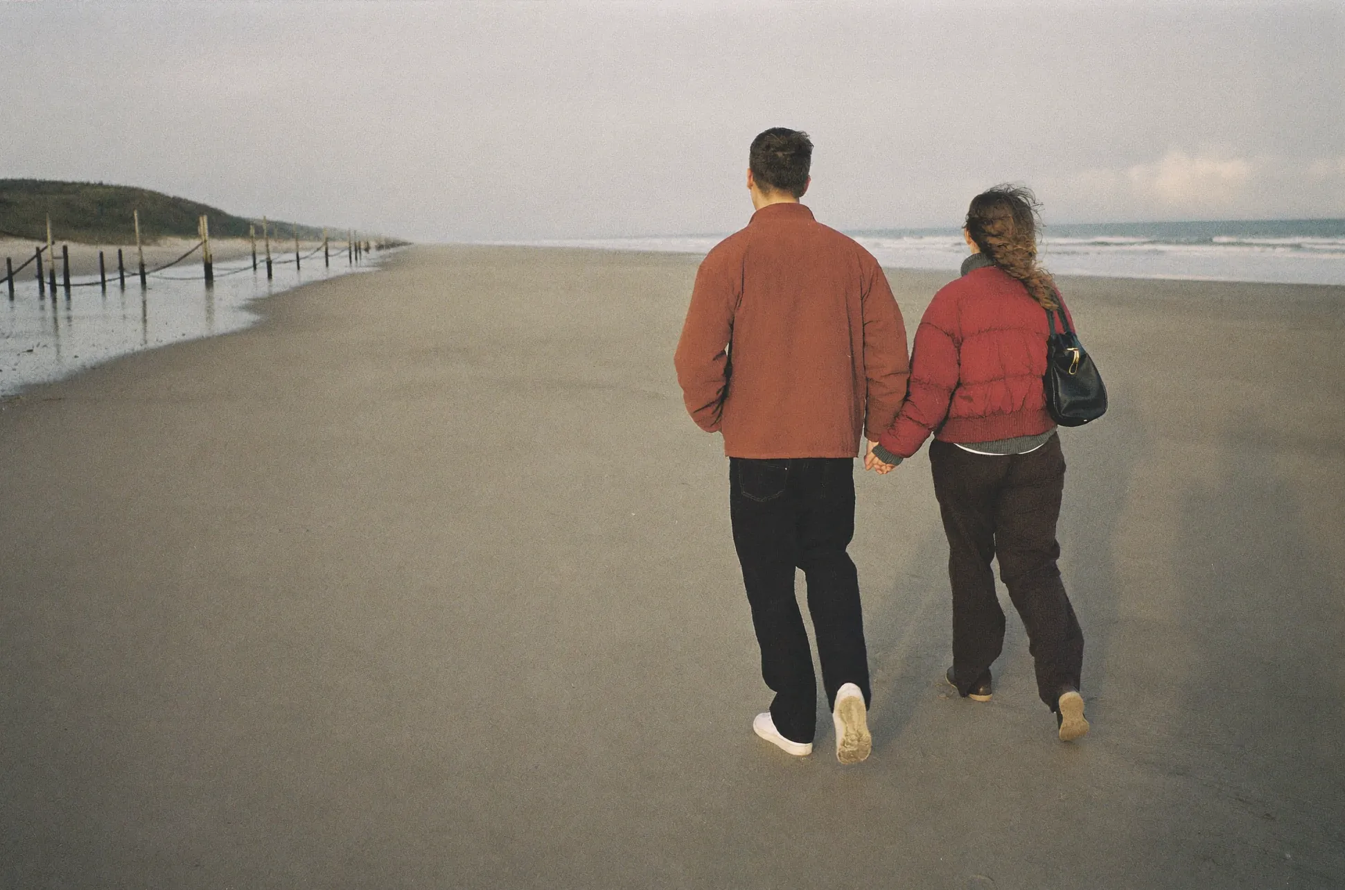 A couple in knitwear walking hand in hand along the tideline of an empty beach